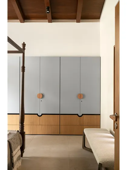 These bespoke wardrobes blend a soft, powdery grey with warm oak. The oversized circular wooden pulls act as modern Kolam-inspired strokes, adding a graphic and tactile detail to the minimalist design.