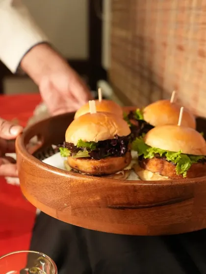 Our staff serving mini burgers from a wooden tray. This is an example of the attentive service we provide at our catered events, ensuring every guest feels welcomed and cared for.