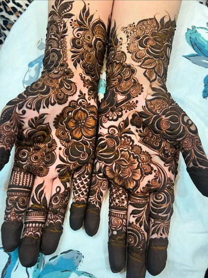 A beautiful example of a complete bridal hand design, with dark fingertips and a dense pattern of flowers and paisleys covering the palms and wrists.