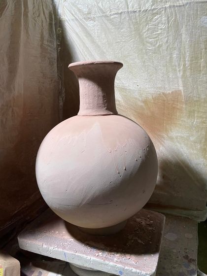 A classic, wheel-thrown vase with a spherical body and a narrow neck. This is a timeless form, shown here in its unfired terracotta clay state.