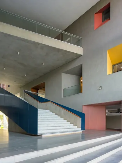 The grand entrance hall of the School of Arts and Sciences at Ahmedabad University. The use of a monumental staircase, double-height spaces, and bold color accents creates a welcoming and impressive point of arrival.