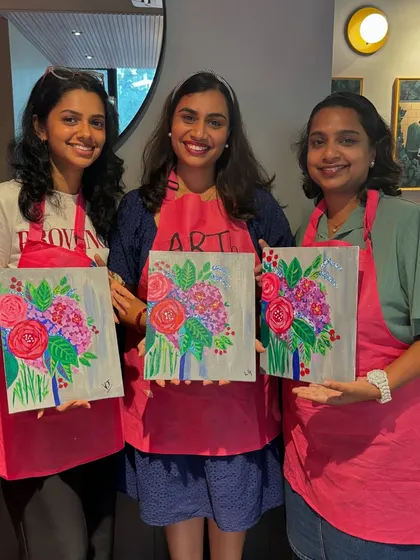 Three friends proudly holding up their matching floral paintings. It's fun to see how each person adds their own unique style to the same subject.