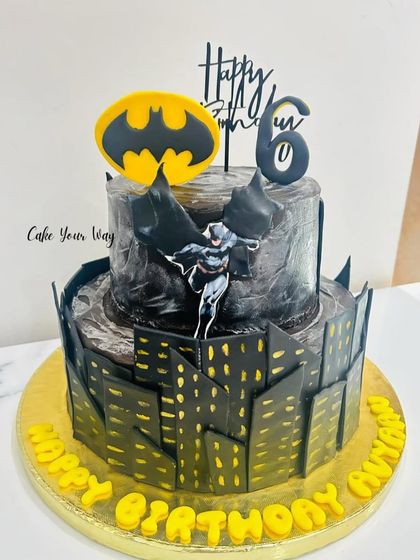 A cake fit for the Dark Knight. This two-tier Batman cake features a Gotham city skyline and the iconic bat signal for a 6th birthday.