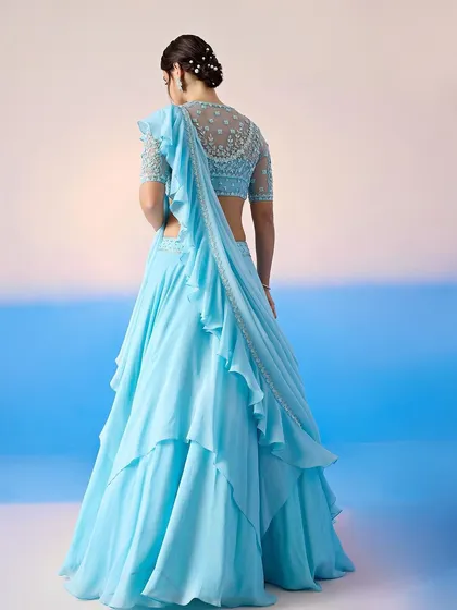 The back of this sky blue lehenga reveals a beautifully embellished blouse and a sheer, ruffled dupatta.
