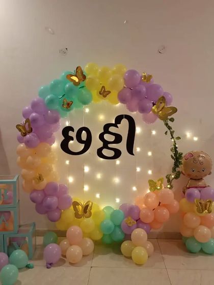 A lovely "Chhathi" ceremony decoration with a pastel-colored balloon ring. The setup is illuminated with fairy lights and includes "BABY" blocks and a balloon pillar with a character foil.