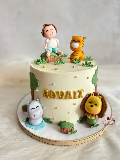 A sweet and simple jungle-themed cake with a personalized sugar figure of the birthday boy sitting with his friends: a tiger, a lion, and a hippo.