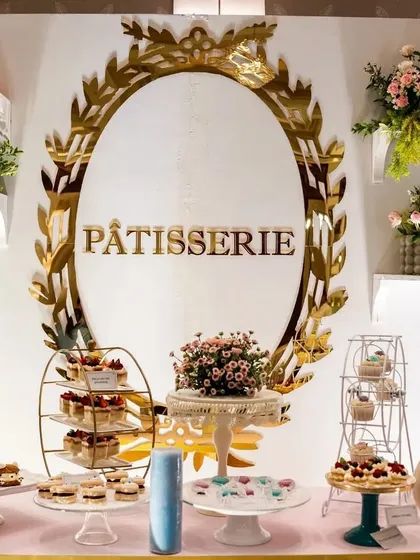 A beautiful Parisian 'Pâtisserie' dessert table. The elegant gold-framed signage, tiered cake stands, and delicate floral arrangements make for a delicious and stylish display.
