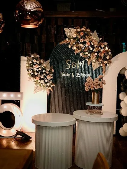 The complete setup for a stylish 25th-anniversary party. The design includes modern furniture, marquee lights, a balloon arch, and sophisticated floral arrangements, creating a perfect ambiance for celebrating a lifetime of love.