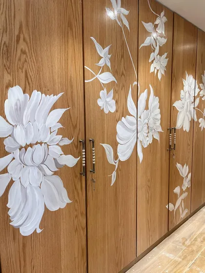 A full view of a wardrobe transformed by art. I painted a cascade of white wildflowers across the wooden shutters, turning a functional storage unit into a beautiful, flowing botanical mural that unifies the entire wall.