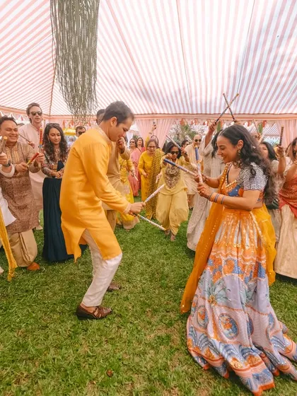 The bride and groom enjoying a Dandiya dance at their Haldi carnival. It's a beautiful way to celebrate their union with a traditional and fun activity.