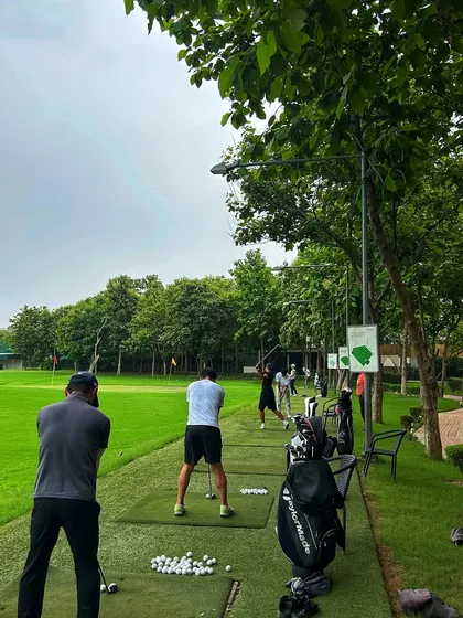A view from behind the tee line, showing a group of golfers practicing together on a cloudy day.