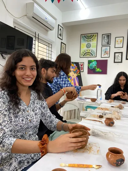 A participant smiles as she sits at a table full of fellow creators in a pottery workshop. The atmosphere is always friendly and supportive.