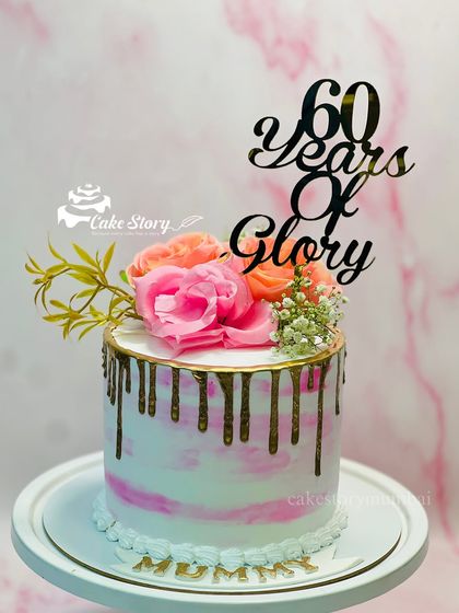 A beautiful cake celebrating '60 Years of Glory' for a mother's birthday. The design features a pink marble effect, a gold drip, and is topped with fresh flowers.