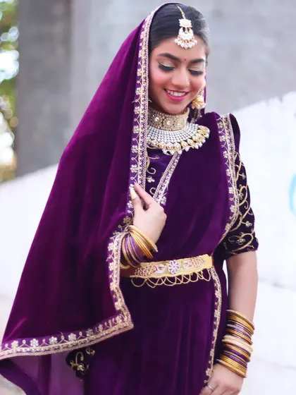 The bride looking down with a gentle smile, her heavy choker and maang tikka completing the royal look.