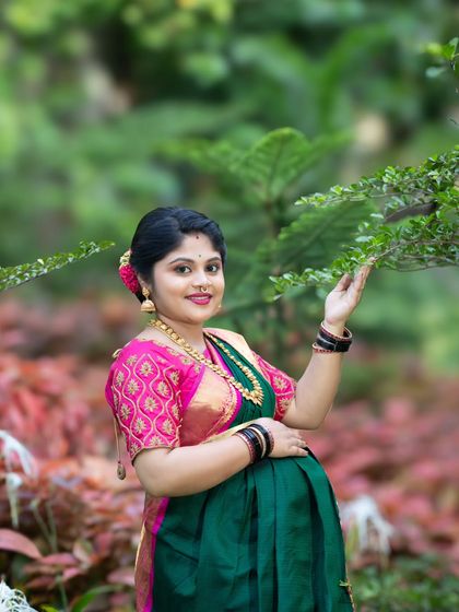 An outdoor maternity shot of a smiling woman in a green and pink saree, interacting with the nature around her in a Bangalore park.
