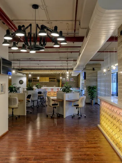 This co-working space reception features hardwood floors and an industrial-style chandelier. The backlit geometric pattern on the desk adds a touch of modern hospitality.