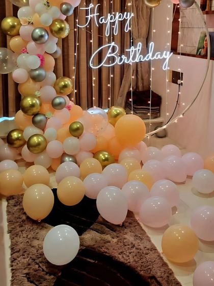 A close-up of a pastel-colored balloon arrangement with a 'Happy Birthday' neon sign and fairy lights. This creates a soft and pretty photo spot.