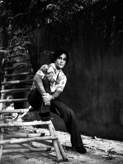 A classic black and white portrait of Zahan Kapoor seated on a bamboo ladder, creating an interesting and rustic composition.