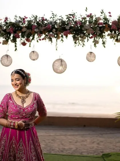 A joyful portrait of the bride at her beachside wedding venue, standing before the beautiful floral arch.