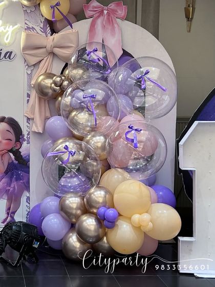 This first birthday setup features a ballerina and butterfly theme with a custom character cutout and a large marquee number '1'. The balloon arrangement uses purple, peach, and metallic gold balloons.