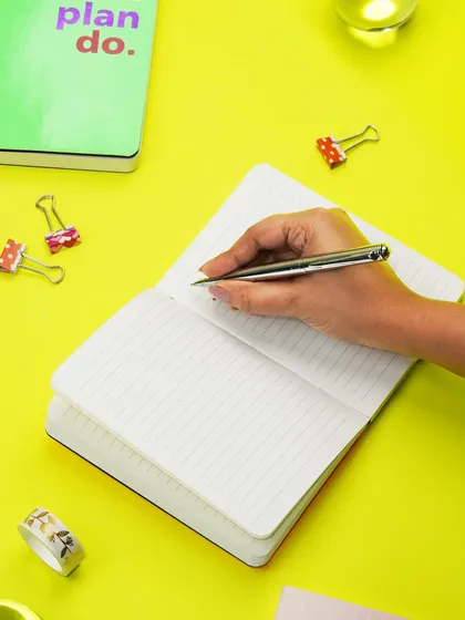 A hand is captured writing in a notebook against a vibrant yellow background. This action shot brings the product to life and highlights its use in a fun, creative context.