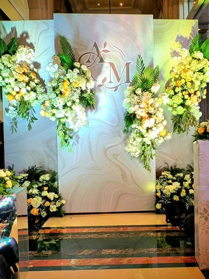 A modern and chic photo backdrop with a marble-finish background, the couple's monogram, and cascading arrangements of white and yellow flowers.