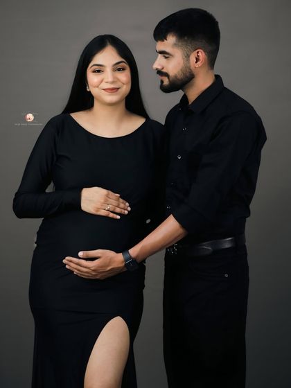 A classic couple's pose where the partner stands beside his wife, his hand gently placed on her bump. Their loving expressions tell a story of shared anticipation.