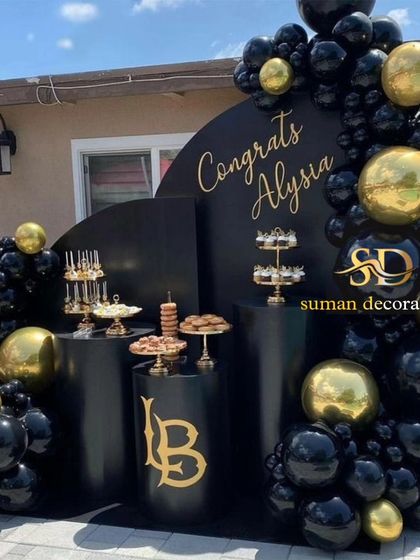 An elegant outdoor graduation or celebration setup in black and gold. This decor features a custom backdrop, multiple dessert pedestals, and a luxurious balloon garland.