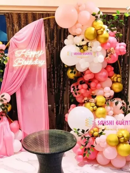A beautiful birthday setup with a pink and gold balloon arch draped with pink fabric.