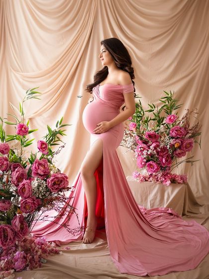 A full-length profile shot that showcases the dramatic slit and train of the pink gown against the lush floral backdrop.