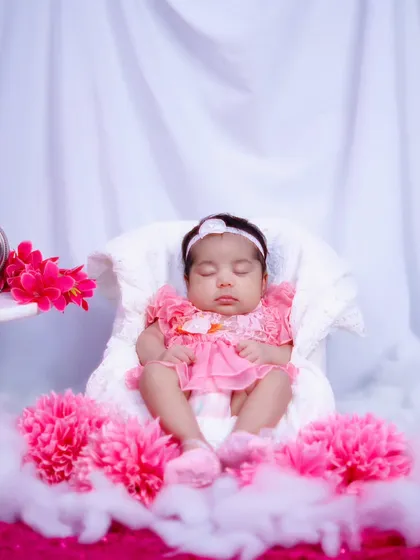 A wider shot of the one-month-old baby girl in her pink dress, surrounded by soft clouds and flowers in a dreamy setup.