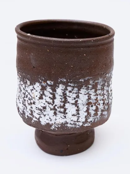 A rustic, hand-formed cup with a textured white glaze applied to the lower half. The form is simple and comfortable to hold.