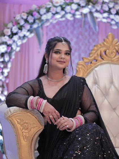 A regal reception look. The bride is seated on a throne-like chair, her black saree and diamond jewelry creating a look of pure elegance.