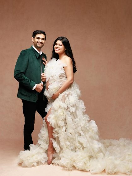 A high-fashion maternity look in the studio. The contrast between the dramatic ruffled gown and the sharp green jacket creates a unique and stylish portrait.