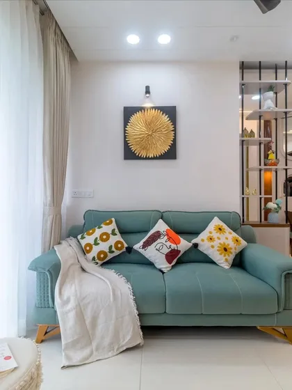 A comfortable and stylish living room with a teal sofa and vibrant cushions. The gold wall art and modern partition add touches of elegance and personality to the space.