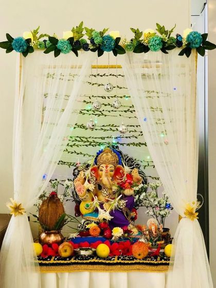 A simple and modern Ganpati decoration with a sheer white canopy and a border of teal-colored flowers. The clean lines and unique color choice make this a fresh and contemporary option.