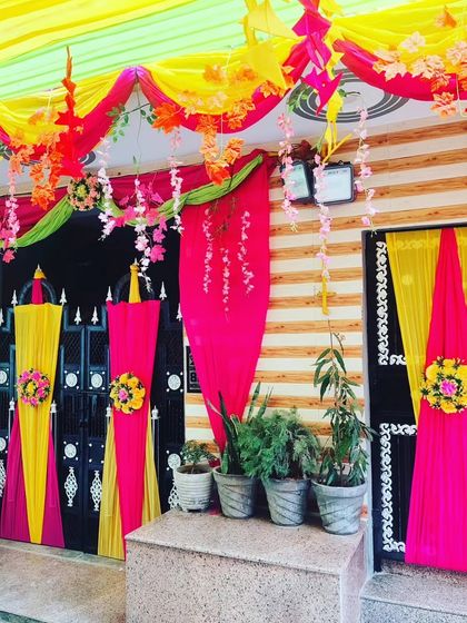 A festive doorway decoration with bright pink and yellow drapes, floral accents, and hanging flower strings.