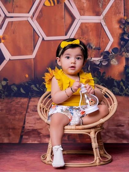 A full view of our bee-themed first birthday setup. This little girl is sitting in a wicker chair, ready to celebrate her special day surrounded by sunflowers and honeycombs.