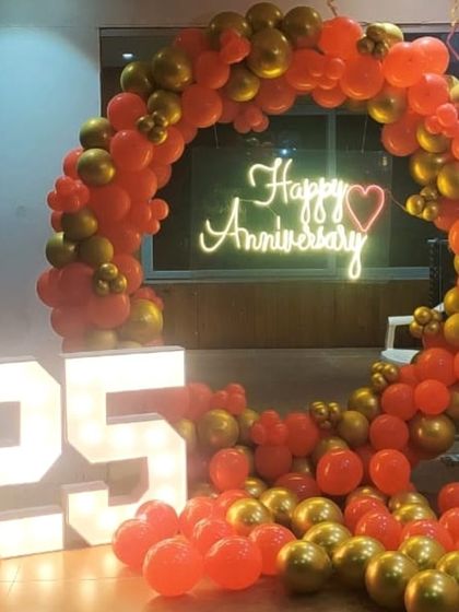 A balloon decoration for a 25th anniversary celebration at home. This setup combines a red and gold balloon arch with large light-up marquee numbers, creating a festive and memorable photo spot.