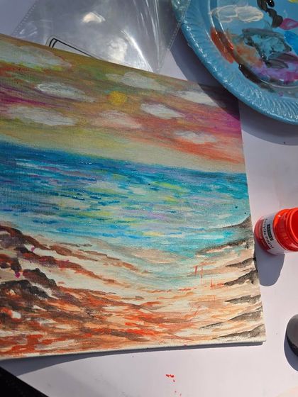 A student's finished seascape painting, with the art supplies used sitting alongside it. Our studio provides a relaxed space where you can unwind and create at your own pace.