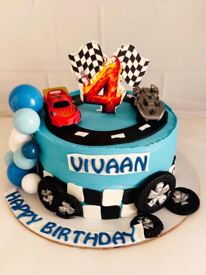 A fun race car-themed cake with a track, checkered flags, and a balloon garland.