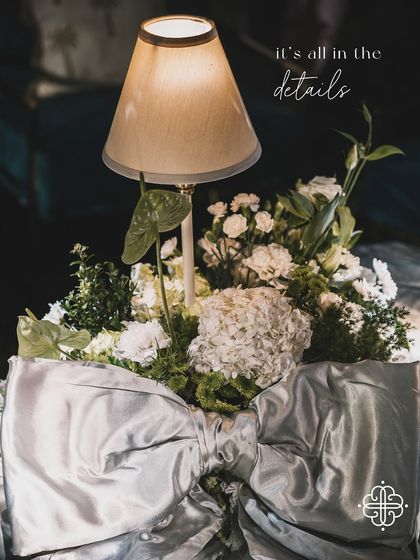A detail of a table centerpiece with a lamp and a large silver bow, with the text overlay "it's all in the details".