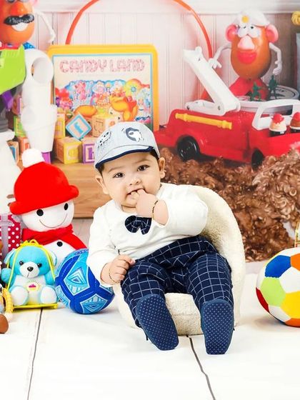 A baby boy in a plaid suit and a cute cap looks thoughtfully at his toys.