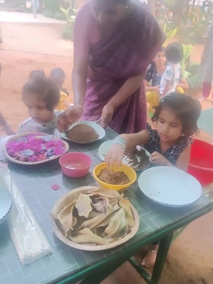 At the creation station, children mix mud and decorate with natural items like leaves and flowers. This is imaginative play at its best.