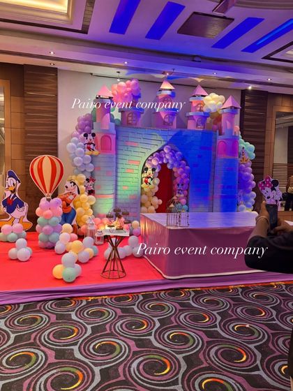 A magical castle theme decoration perfect for a fairytale birthday. This setup features a large castle prop with a balloon arch, character cutouts like Donald Duck, and a small table for the cake.