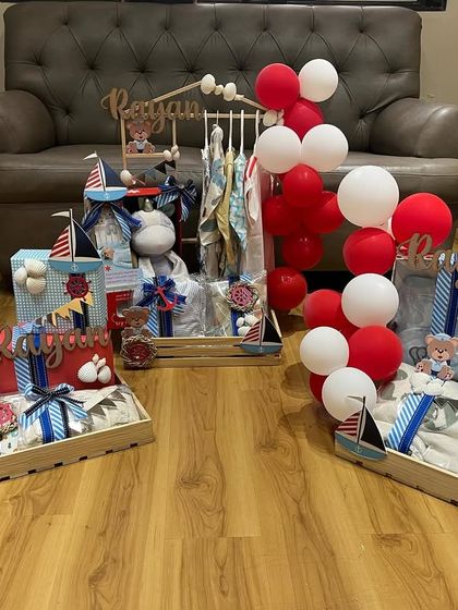 Welcoming a little sailor with a gorgeous set of gift hampers. This baby trousseau features a nautical theme with boats, anchors, and a red, white, and blue color scheme, complete with personalized name displays.