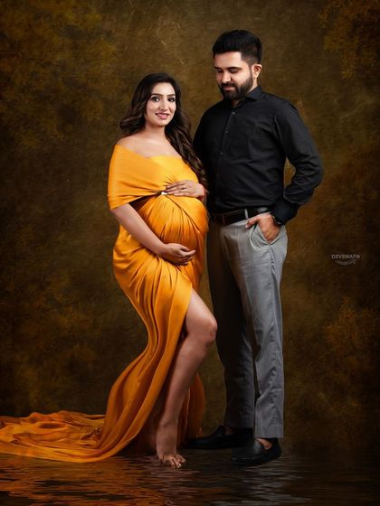 A beautiful couple portrait with a warm, golden color palette. The client's mustard gown and her partner's dark outfit create a lovely contrast against the painterly backdrop.