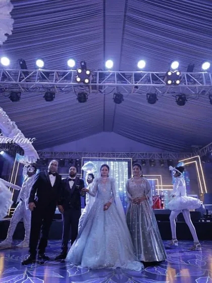 A modern, fairytale sangeet entry. The couple is surrounded by performers in ethereal, ballet-inspired costumes, creating a dreamy and sophisticated atmosphere under the stage lights.