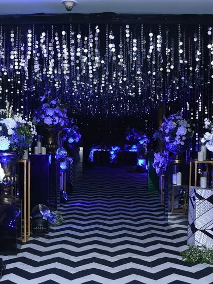 This entrance makes a bold statement with a black-and-white chevron carpet, a tunnel of hanging crystals, and dramatic blue uplighting.