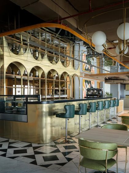 The central bar at Citadines is a striking focal point, with a polished brass front and olive-green leather stools. Mirrored panels on the ceiling above reflect the activity below, enhancing the sense of space and energy.